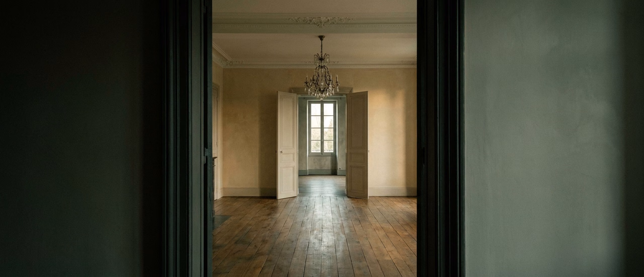 Enfilade de trois pièces d'une maison de maître en basse lumière, portes alignées jusqu'à une fenêtre lointaine